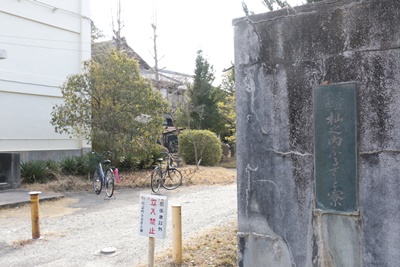 入り口の門標。現在は、周囲に建物や植え込みがあり、建築当初のように全体を見渡すことができない。左側の白い建物が北寮。奧に本館がみえる。（2021年2月10日撮影）