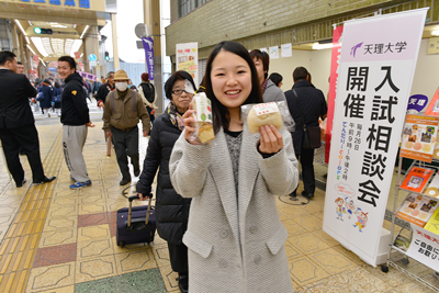 「トマトン」と「ベジケーキ」を手に呼び込みをする学生